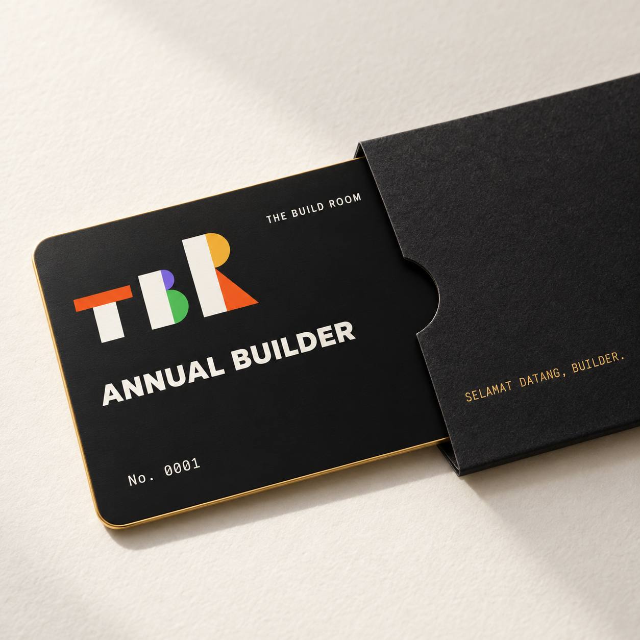 Kartu member logam hitam bertuliskan ANNUAL BUILDER No. 0001, setengah keluar dari sampul hitam.
