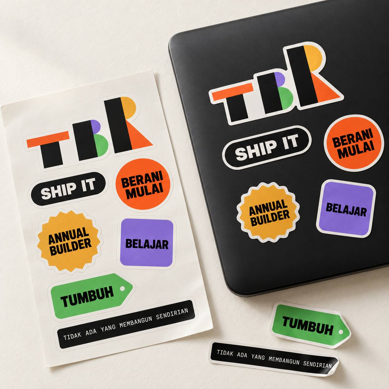 Lembar stiker TBR dengan logo, SHIP IT, BERANI MULAI, ANNUAL BUILDER, BELAJAR, dan TUMBUH, sebagian tertempel di laptop hitam.